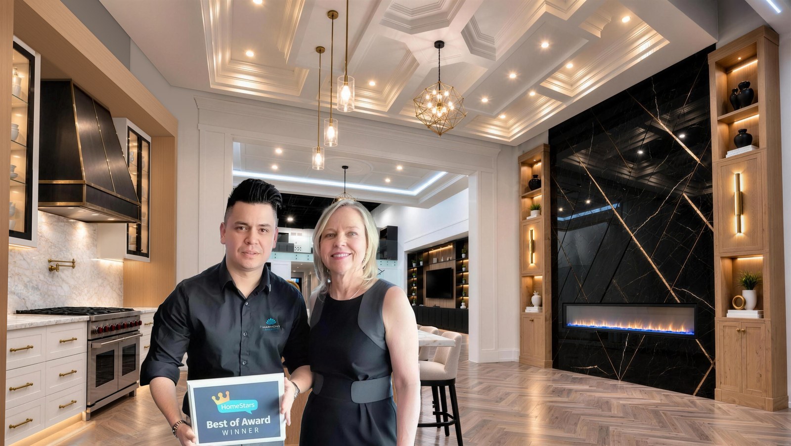 Diego Botia and Nancy Peterson of HomeStars holding the HomeStars Best of Award in the Harmony Basements Vaughan design centre, under the coffered ceiling, between the white-oak kitchen and the black marble fireplace wall