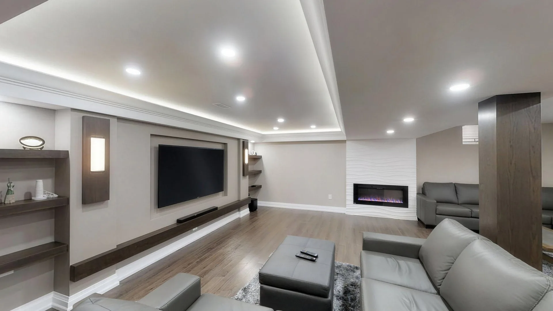 A finished Harmony basement seen from the middle of the room: the recessed media wall, the grey sectional and the white wave-panel fireplace wall under a cove-lit ceiling