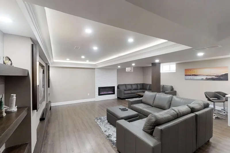 Finished basement in Toronto: grey sectional, linear fireplace wall and a bar with stools, in the 3D tour